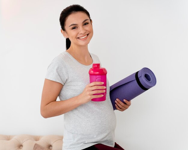 Smiley femme enceinte tenant un tapis de fitness et une bouteille d'eau