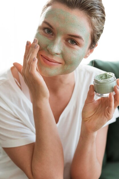 Smiley femme avec masque facial tenant un récipient cosmétique