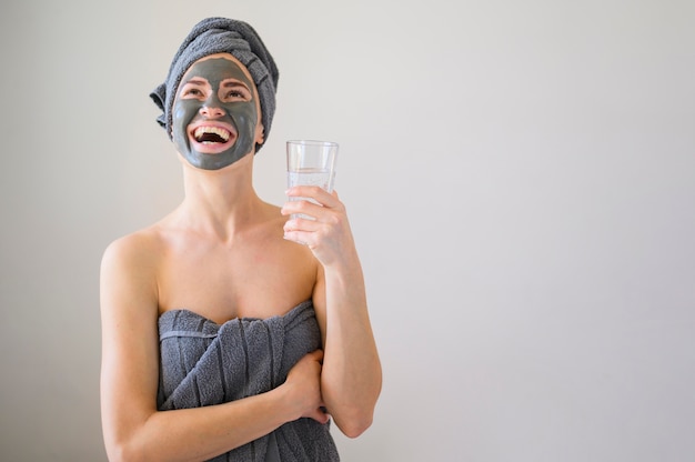 Smiley femme avec masque facial sur tenant un verre d'eau