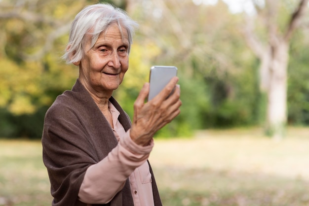 Smiley femme plus âgée tenant le smartphone à l'extérieur