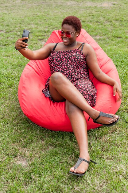 Smiley femme prenant selfie sur sac de haricots à l'extérieur