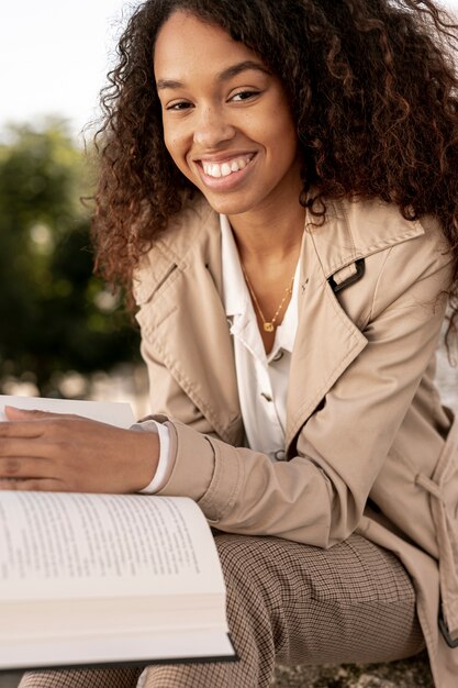 Smiley femme tenant un livre ouvert à l'extérieur