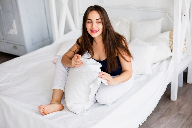 Smiley femme tenant oreiller dans son lit