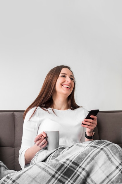 Smiley femme tenant un smartphone et une tasse