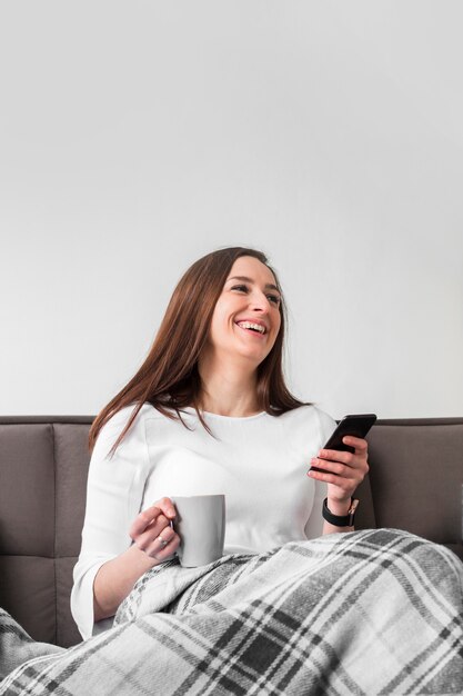 Smiley femme tenant un smartphone et une tasse