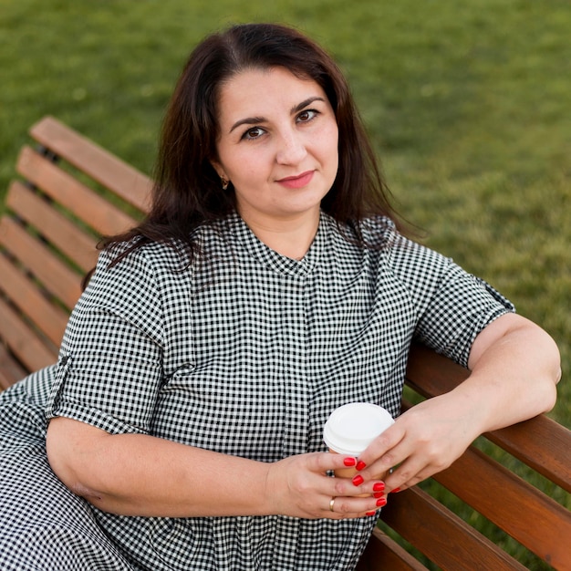 Smiley femme tenant une tasse de café assis sur un banc