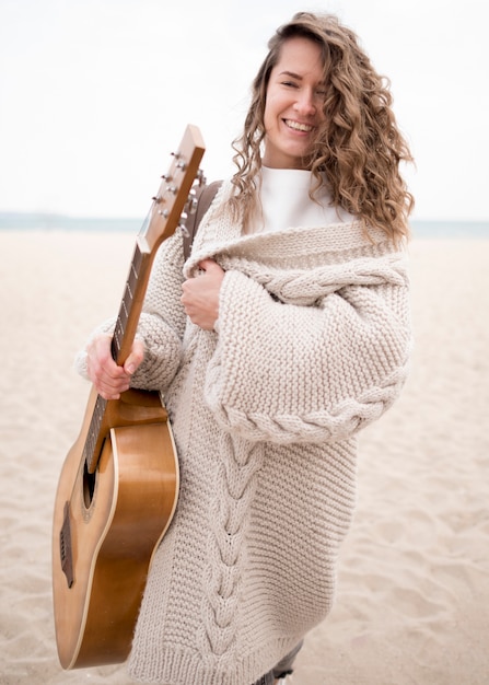 Photo gratuite smiley girl tenant une guitare sur la plage