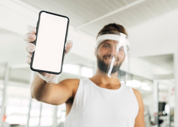 Smiley homme avec écran facial à la salle de gym holding smartphone