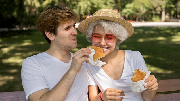 Smiley jeune couple de manger des hamburgers dans le parc