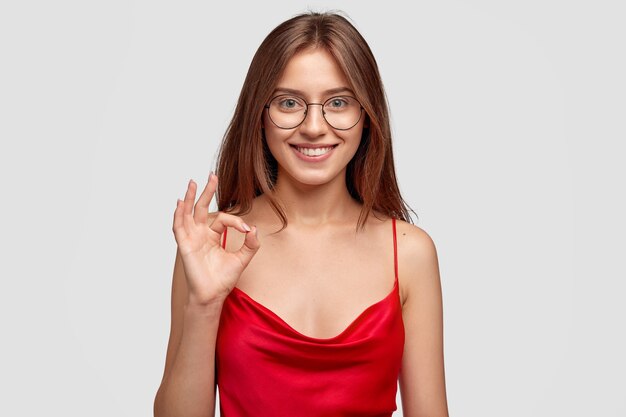 Smiley jeune femme brune posant contre le mur blanc