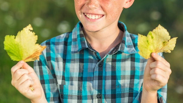 Photo gratuite smiley jeune garçon mains avec feuilles d'automne