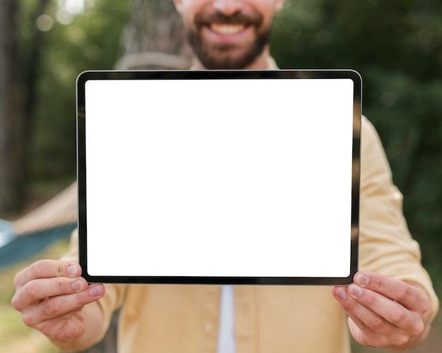 Smiley man holding up tablet en camping en plein air