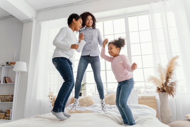 Smiley mère sautant dans son lit à la maison avec ses enfants