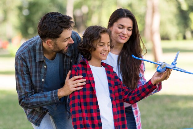 Smiley parents et enfant jouant avec avion ensemble à l'extérieur