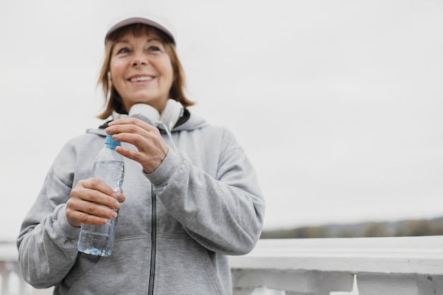 Smiley senior woman avec bouteille d'eau et casque à l'extérieur