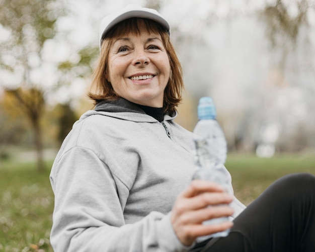 Smiley senior woman eau potable à l'extérieur après avoir travaillé