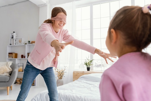 Smiley sisters jouant à la maison avec les yeux bandés