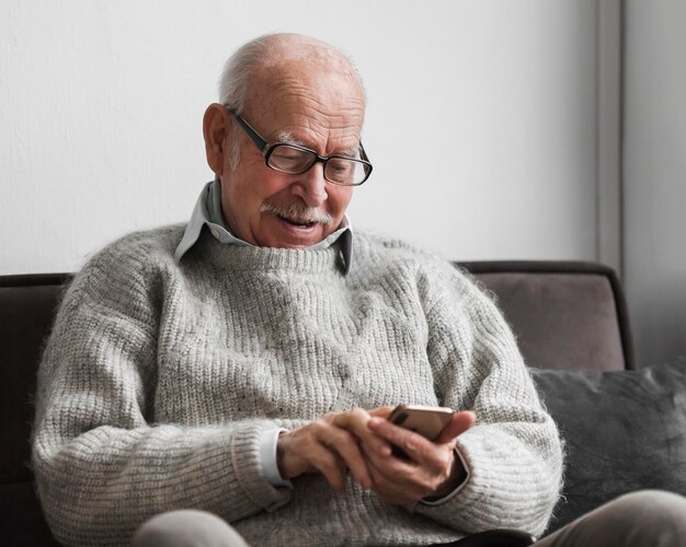 Smiley vieil homme à l'aide de smartphone dans une maison de soins infirmiers