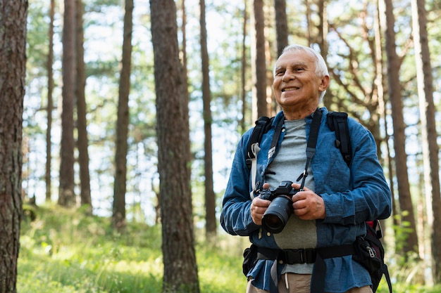 Photo gratuite smiley vieil homme explorant la nature avec appareil photo