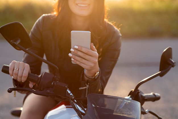 Photo gratuite smiley woman looking at smartphone alors qu'il était assis sur sa moto