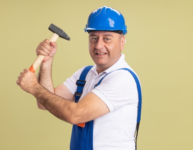 Smiling adult builder homme en uniforme tient un marteau sur vert olive