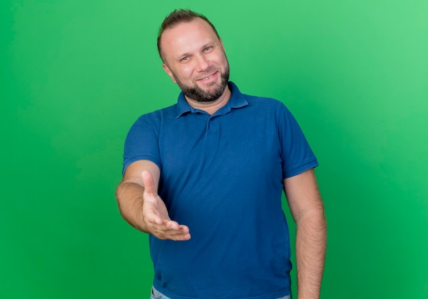 Smiling adult slavic man stretching out hand doing hi geste isolé sur un mur vert avec copie espace