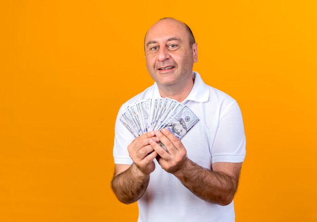 Smiling casual man holding cash isolé sur mur jaune