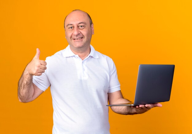 Smiling casual man holding dossier son pouce vers le haut isolé sur mur jaune