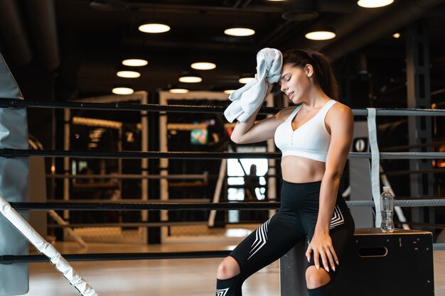 Smiling fit girl holding serviette et prendre du repos dans la salle de gym Fille essuie la sueur avec une serviette