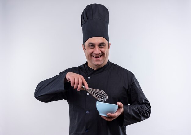 Smiling male d'âge moyen cuisinier en uniforme de chef tenant un fouet avec un bol