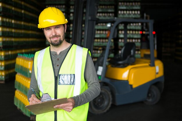 Smiling male worker écrit sur le presse-papiers dans l'entrepôt