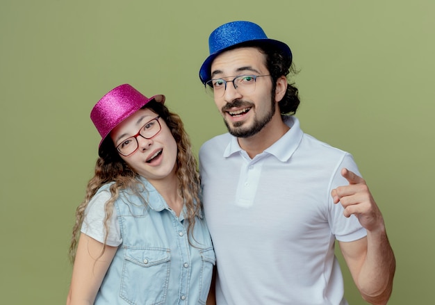 Smiling young couple wearing pink et blue hat guy vous montrant le geste isolé sur vert olive