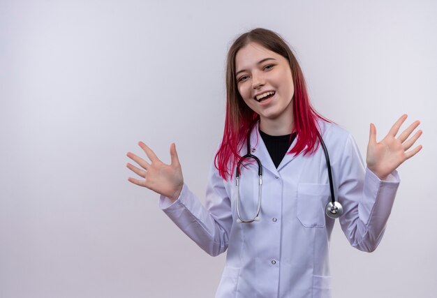 Smiling young doctor girl wearing stéthoscope robe médicale se propage les mains sur fond blanc isolé