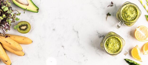 Smoothie vert de légumes et de fruits avec des ingrédients dans des bocaux en verre sur fond blanc, vue de dessus, espace de copie. bannière