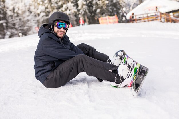Snowboarder est assis haut dans les montagnes sur le bord de la pente et regarde la caméra avant de rouler