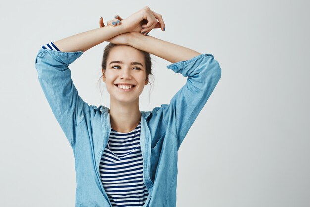 Sœur se souvenait de souvenirs amusants. Portrait intérieur de jolie femme créative tenant les bras croisés sur le front tout en souriant, en regardant de côté, en étant heureux, debout en tenue à la mode