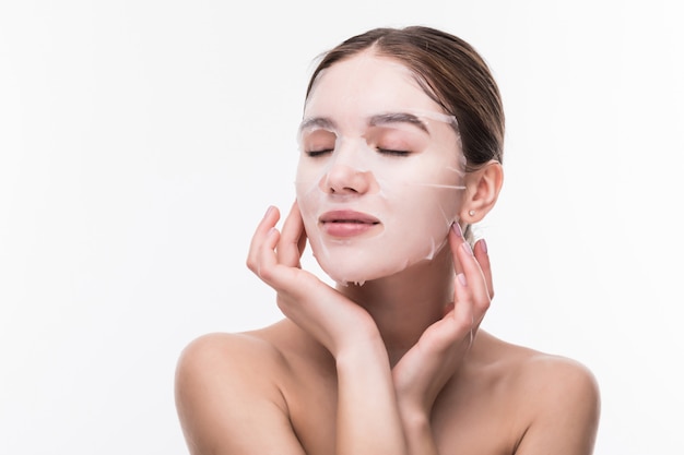 Soins du visage et soins de beauté. Jeune femme avec un masque hydratant en tissu sur son visage isolé sur mur gris