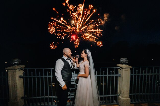 Le soir, un couple avec des lunettes se tient debout et regarde les feux d'artifice de leur mariage