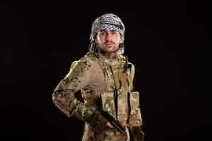 Photo gratuite soldat masculin en camouflage combattant avec une arme à feu sur un mur noir