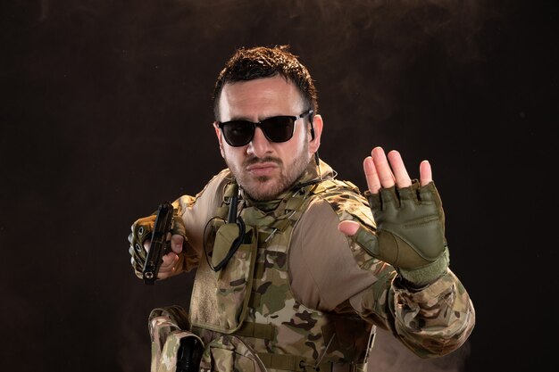 Soldat masculin en camouflage combattant avec un pistolet sur un mur sombre