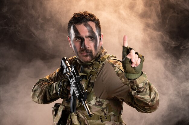 Soldat masculin en tenue de camouflage avec mitrailleuse sur le mur enfumé sombre