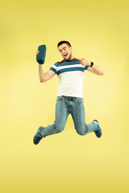 Son du ciel. Portrait en pied d'un homme sautant heureux avec des gadgets sur fond jaune. Technologie moderne, concept de liberté de choix, concept d'émotions. Utilisation d'un haut-parleur portable comme un super-héros en vol.
