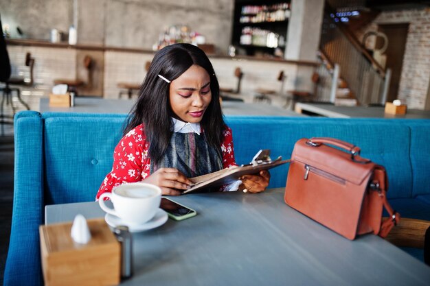 Sonfident jeune femme afro-américaine en tenue décontractée intelligente au café lire le menu