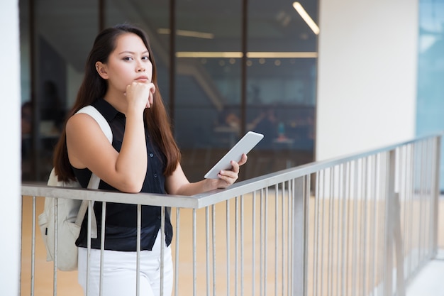 Songeuse jeune femme avec tablette pc regardant la caméra