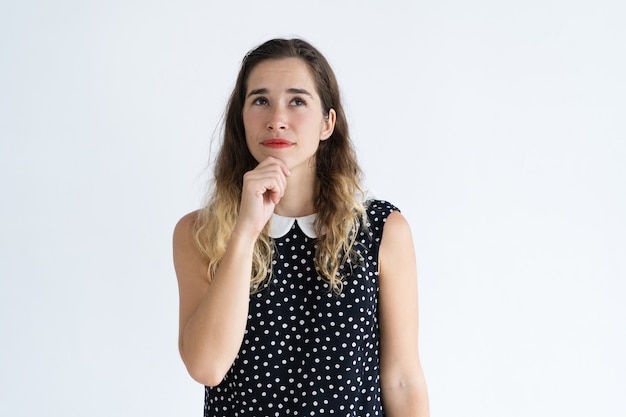 Songeuse jeune femme touchant le menton et levant les yeux