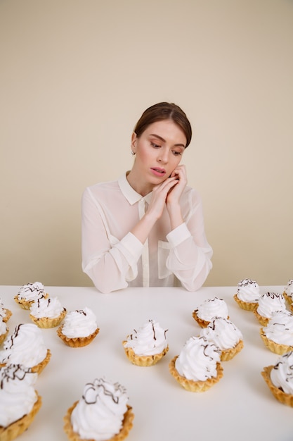 Songeuse jolie jeune femme assise à la table avec des gâteaux