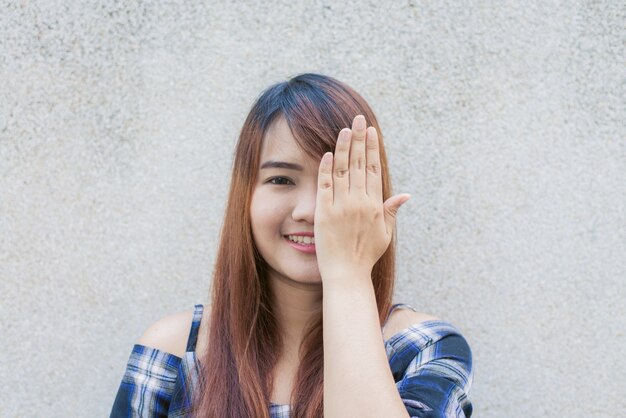 Sonriendo joven hermosa mujer asiática cerrar los ojos con las manos en el fondo de muro de hormigón. Vintage efecto de estilo pictures.miling joven hermosa mujer asiática cerrar los ojos con las manos en el fondo de muro de hormigón. Vintage efecto estilo imágenes.