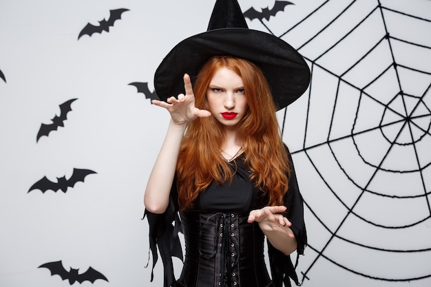 Sorcière Halloween concept pleine longueur sorcière halloween sorts avec une expression sérieuse sur mur gris foncé avec chauve-souris et toile d'araignée