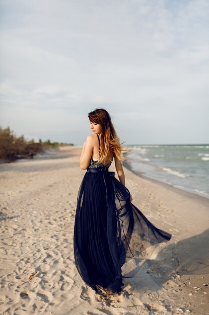 Sortie de femme gracieuse dans une élégante longue robe bleue s'amuser et s'amuser sur la plage tropicale. Temps de vacances