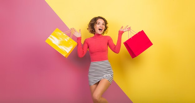 Sortie jolie femme en tenue colorée élégante tenant des sacs à provisions avec expression de visage surpris